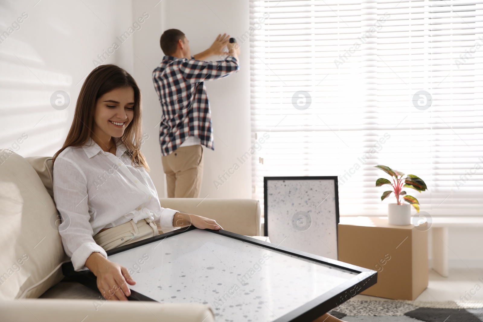 Photo of Happy couple decorating room with pictures together. Interior design