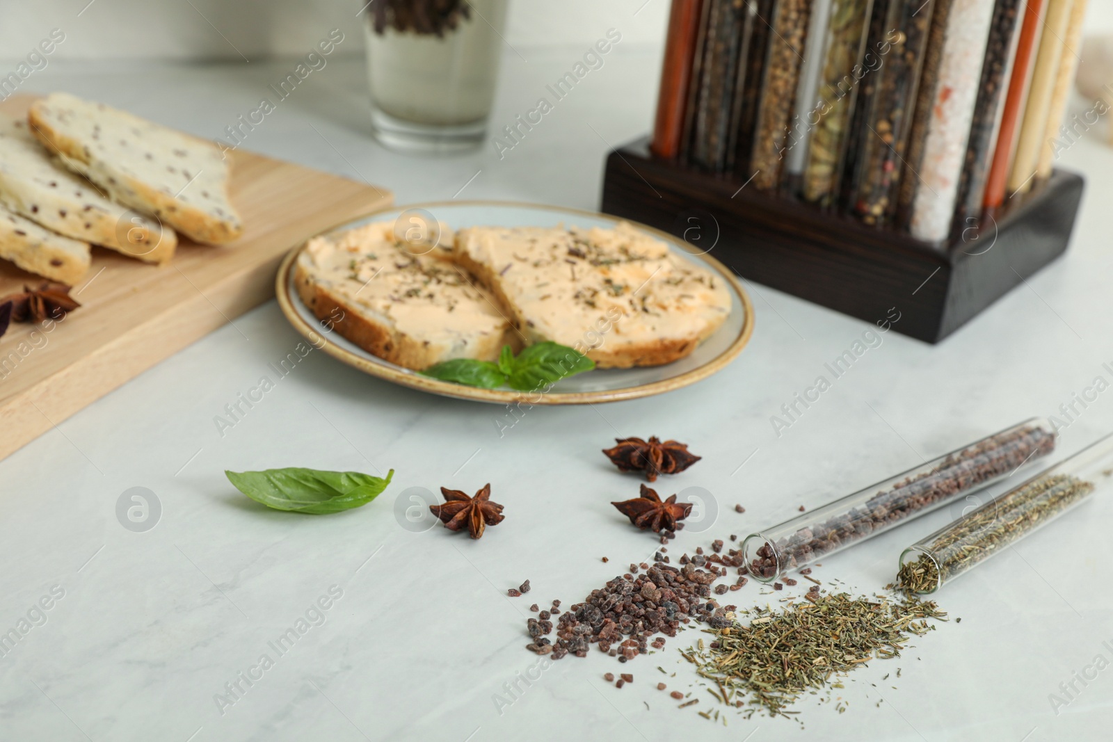 Photo of Glass tubes with black salt and Italian herb mix near plate of sandwiches on kitchen counter