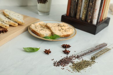 Photo of Glass tubes with black salt and Italian herb mix near platesandwiches on kitchen counter