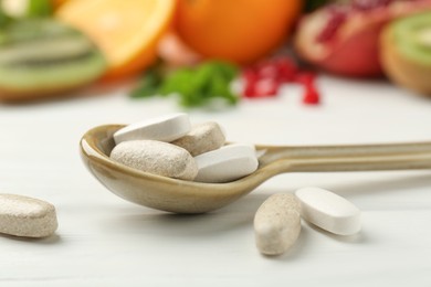 Photo of Different vitamin pills in spoon and fresh fruits on white wooden table, closeup