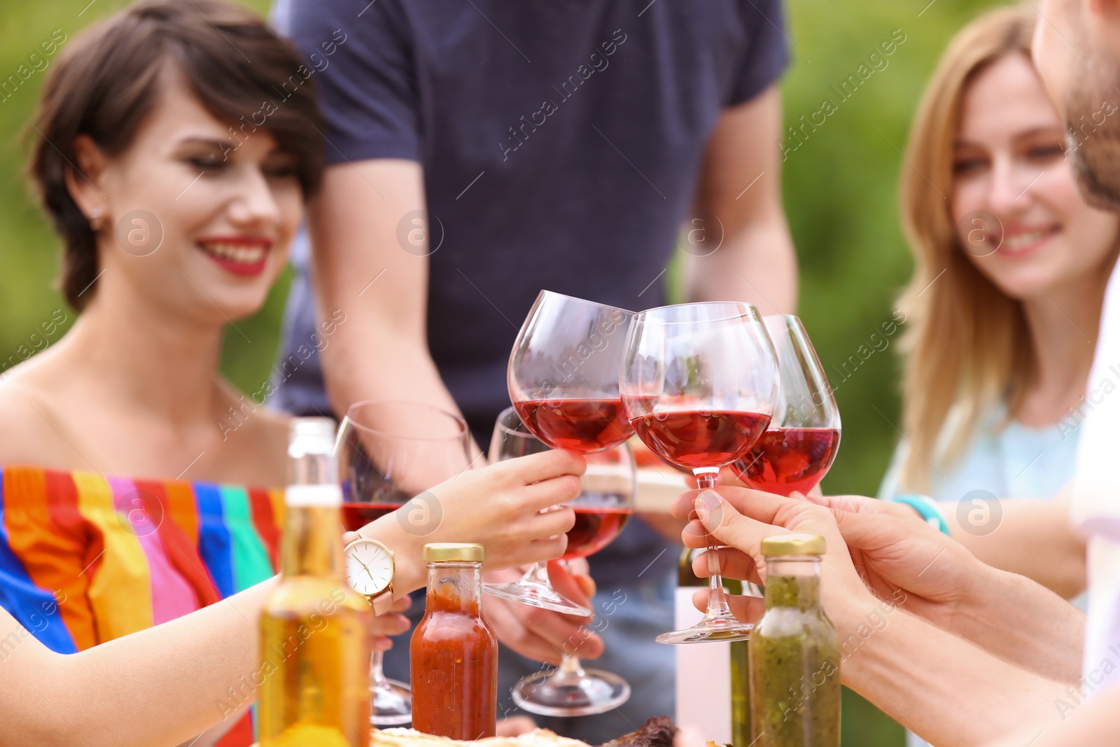 Photo of Young people with glasses wine at table outdoors. Summer barbecue