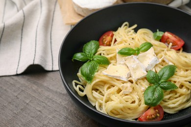 Photo of Delicious pasta with brie cheese, tomatoes and basil leaves on wooden table, closeup. Space for text