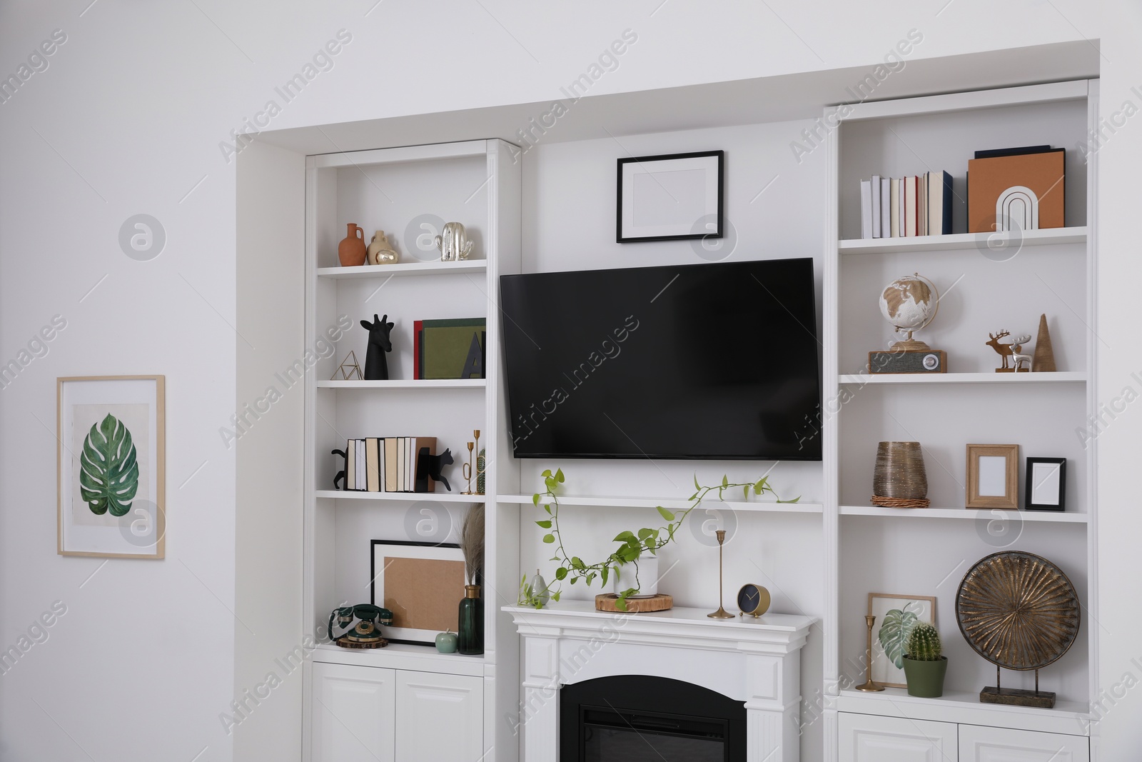 Photo of Stylish shelves with different decor elements, fireplace and TV set in living room. Interior design