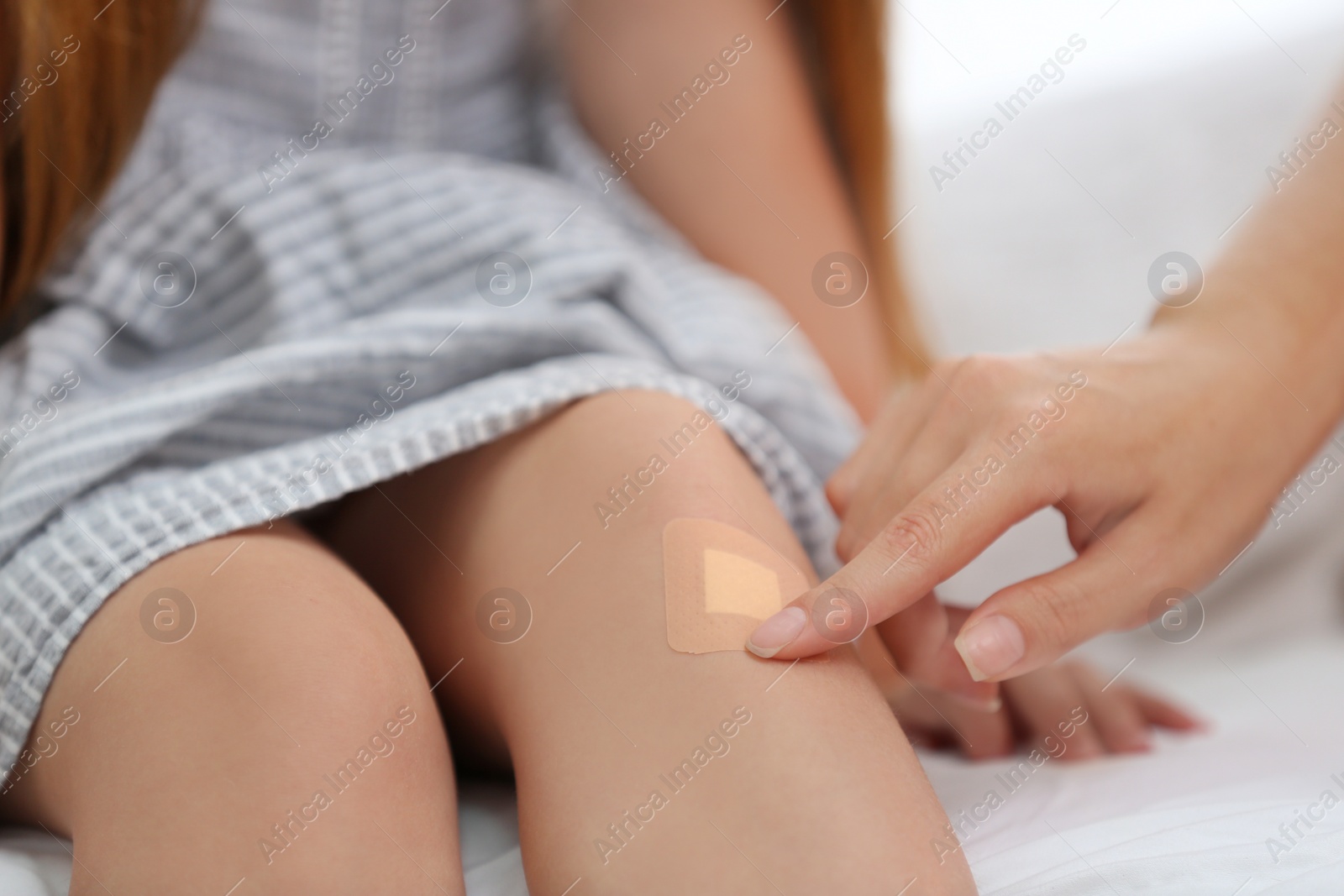 Photo of Woman applying plaster on girl's knee, closeup view