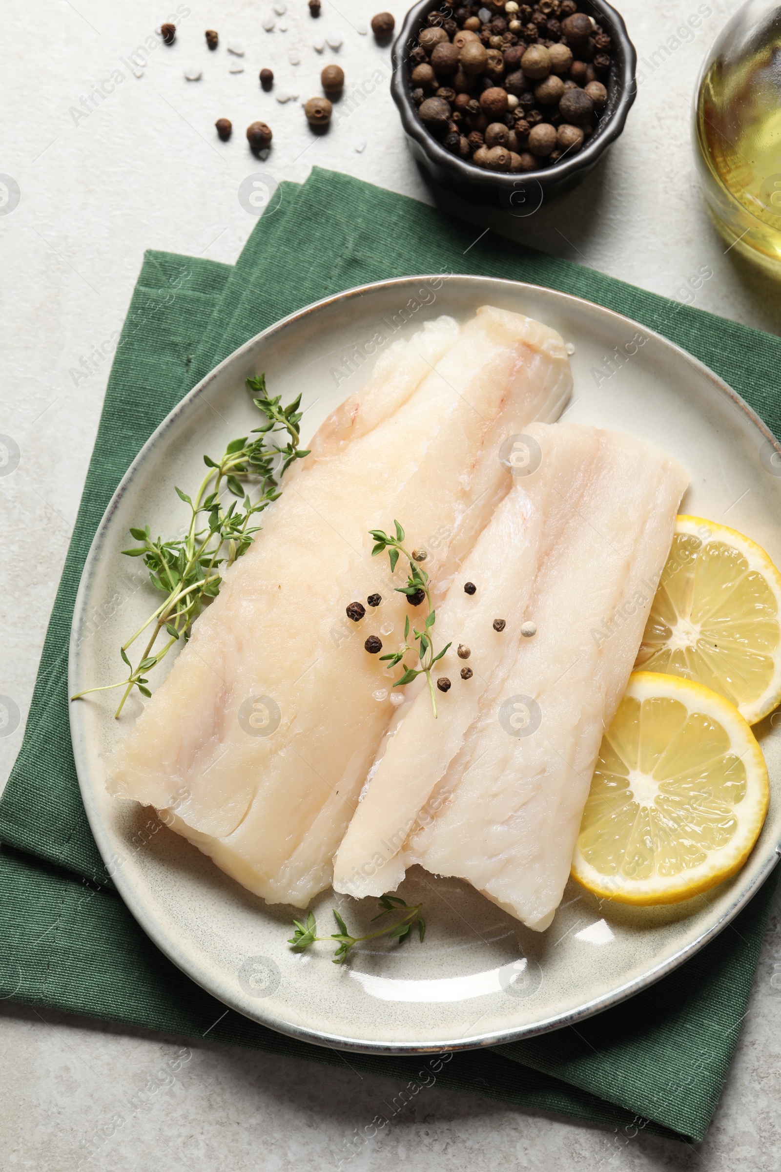 Photo of Plate with raw cod fish, spices, microgreens and lemon on grey table, flat lay