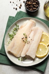 Plate with raw cod fish, spices, microgreens and lemon on grey table, flat lay