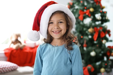 Photo of Cute little child in Santa hat at home. Christmas celebration