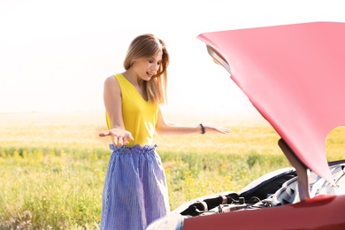 Stressed woman standing near broken car in countryside