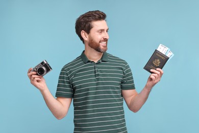 Smiling man with passport, camera and tickets on light blue background