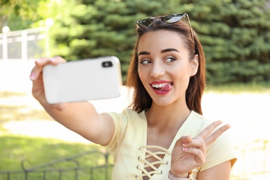 Photo of Young woman taking selfie outdoors on sunny day
