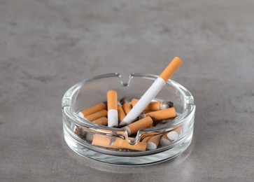 Photo of Glass ashtray with cigarette butts on grey table. Space for text