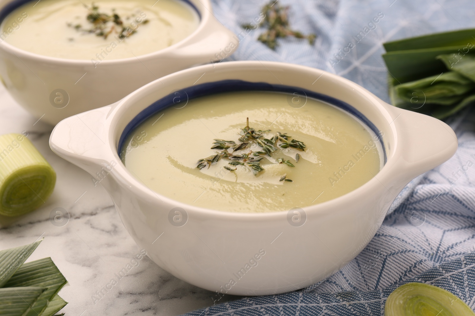 Photo of Tasty leek soup in bowls on white marble table, closeup