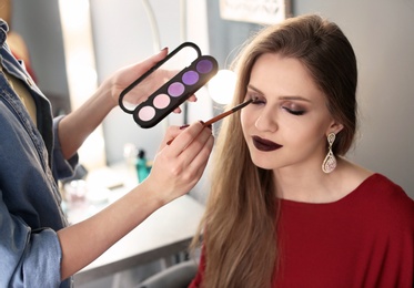 Professional makeup artist working with beautiful young woman in studio