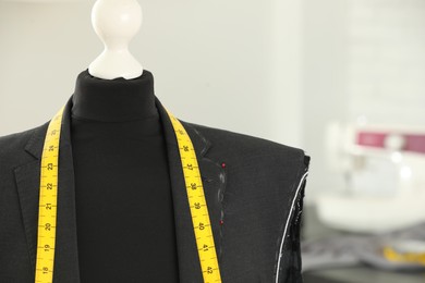 Mannequin with unfinished jacket and measuring tape in tailor shop, closeup. Space for text