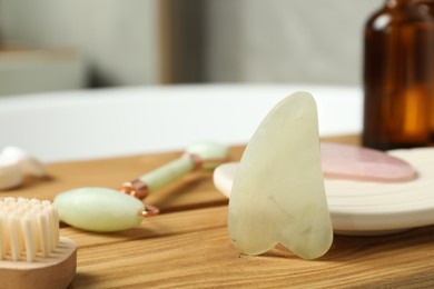 Photo of Jade and rose quartz gua sha tools, natural face roller with cosmetic product on wooden bath caddy, closeup