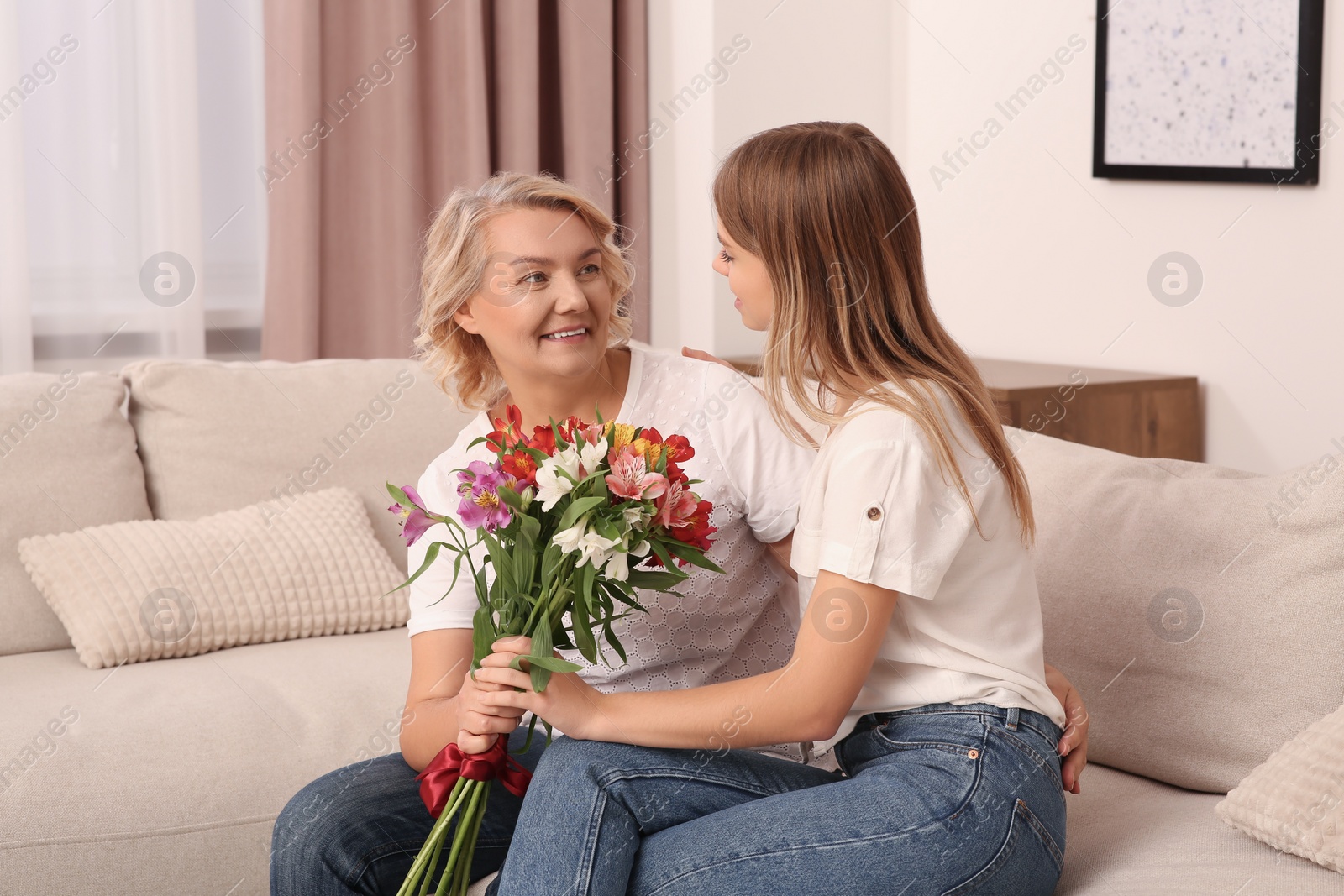 Photo of Young daughter congratulating her mom with flowers at home. Happy Mother's Day