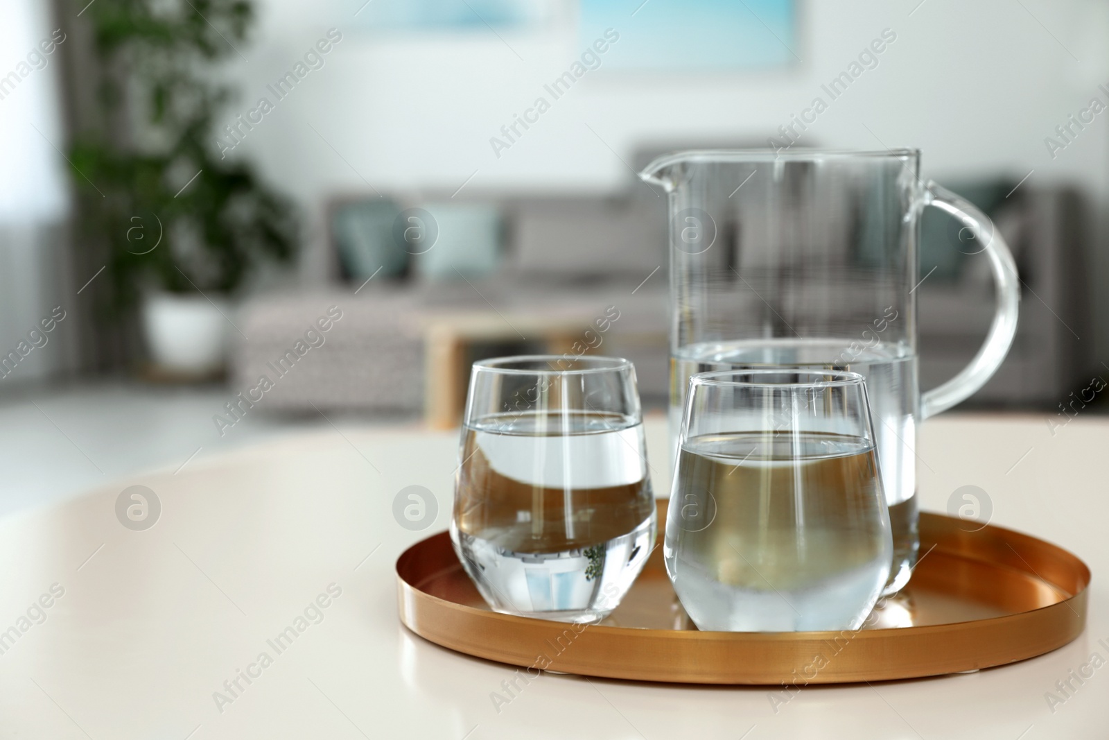 Photo of Tray with jug and glasses of water on white table in room, space for text. Refreshing drink