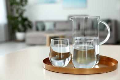 Tray with jug and glasses of water on white table in room, space for text. Refreshing drink