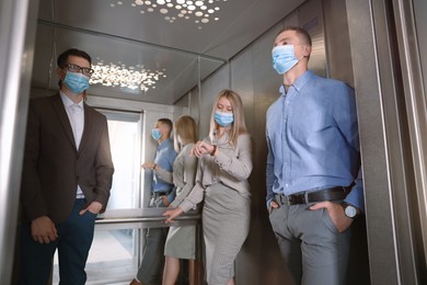 Photo of Group of people with face masks in elevator. Protective measure