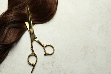 Professional hairdresser scissors with brown hair strand on grey table, top view. Space for text