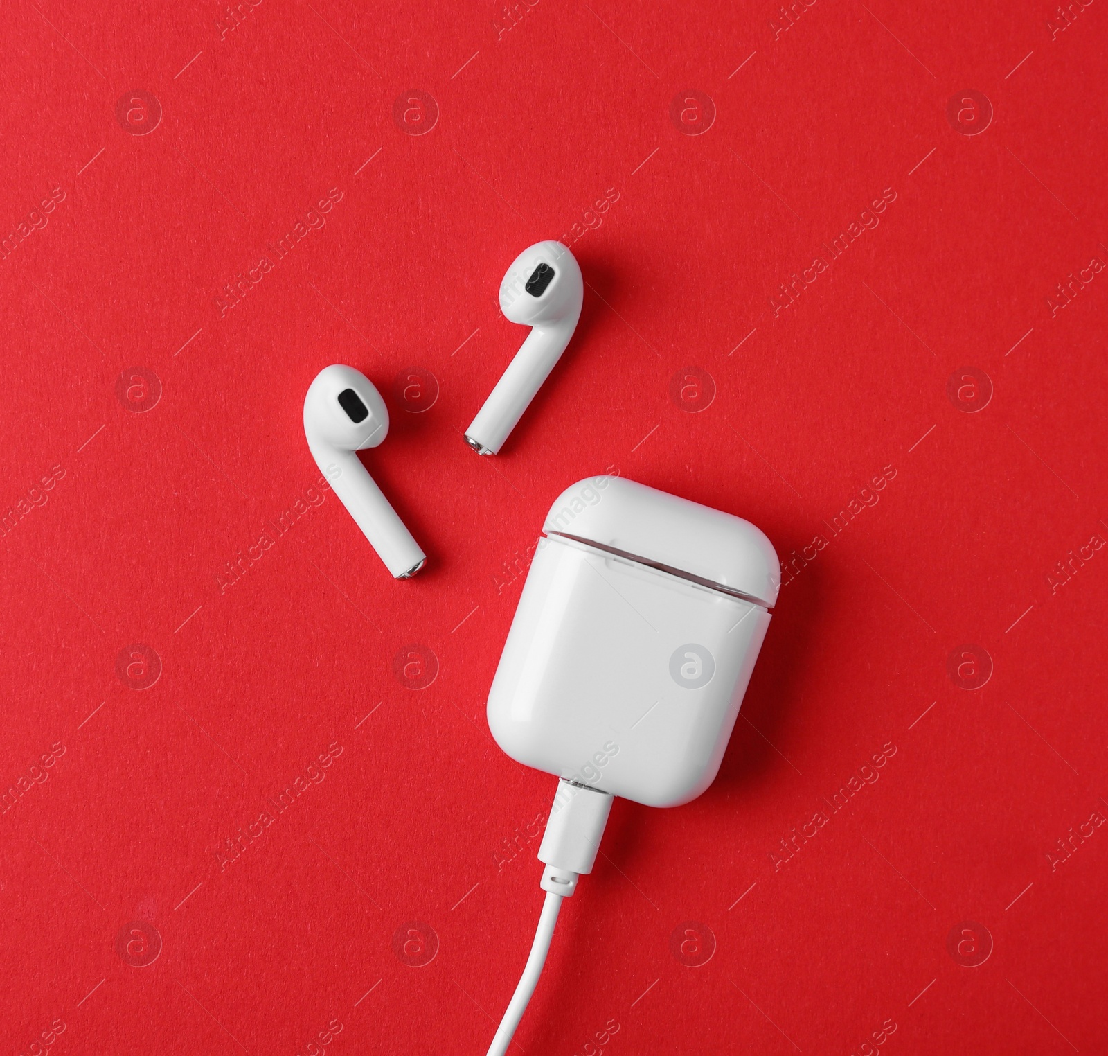 Photo of Modern wireless earphones and charging case with cable on red background, flat lay