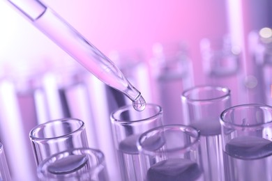 Photo of Dripping liquid from pipette into test tube on violet background, closeup