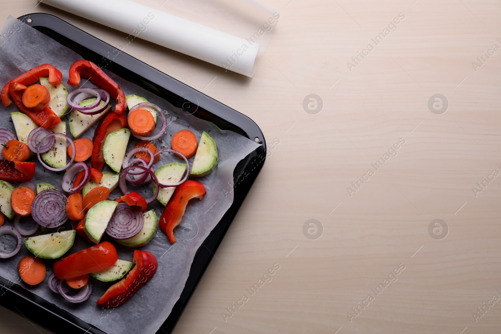 Photo of Baking pan with raw vegetables and parchment paper on wooden table, flat lay. Space for text