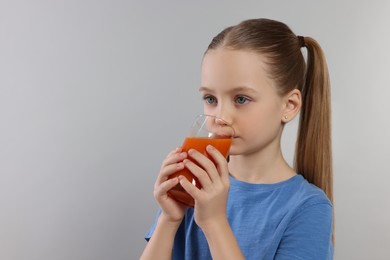 Photo of Cute little girl drinking fresh juice on light gray background, space for text