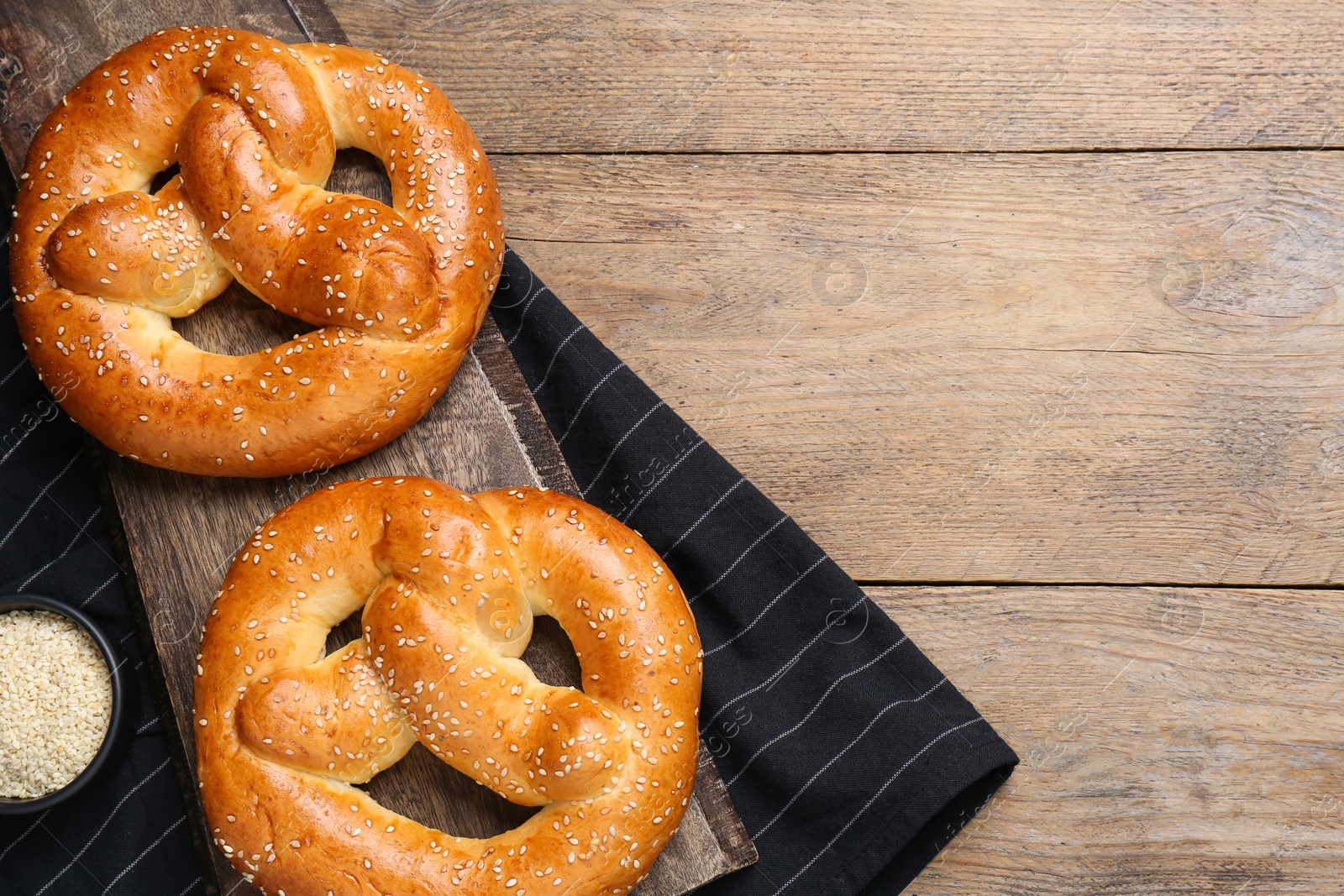 Photo of Delicious pretzels and bowl with sesame seeds on wooden table, flat lay. Space for text