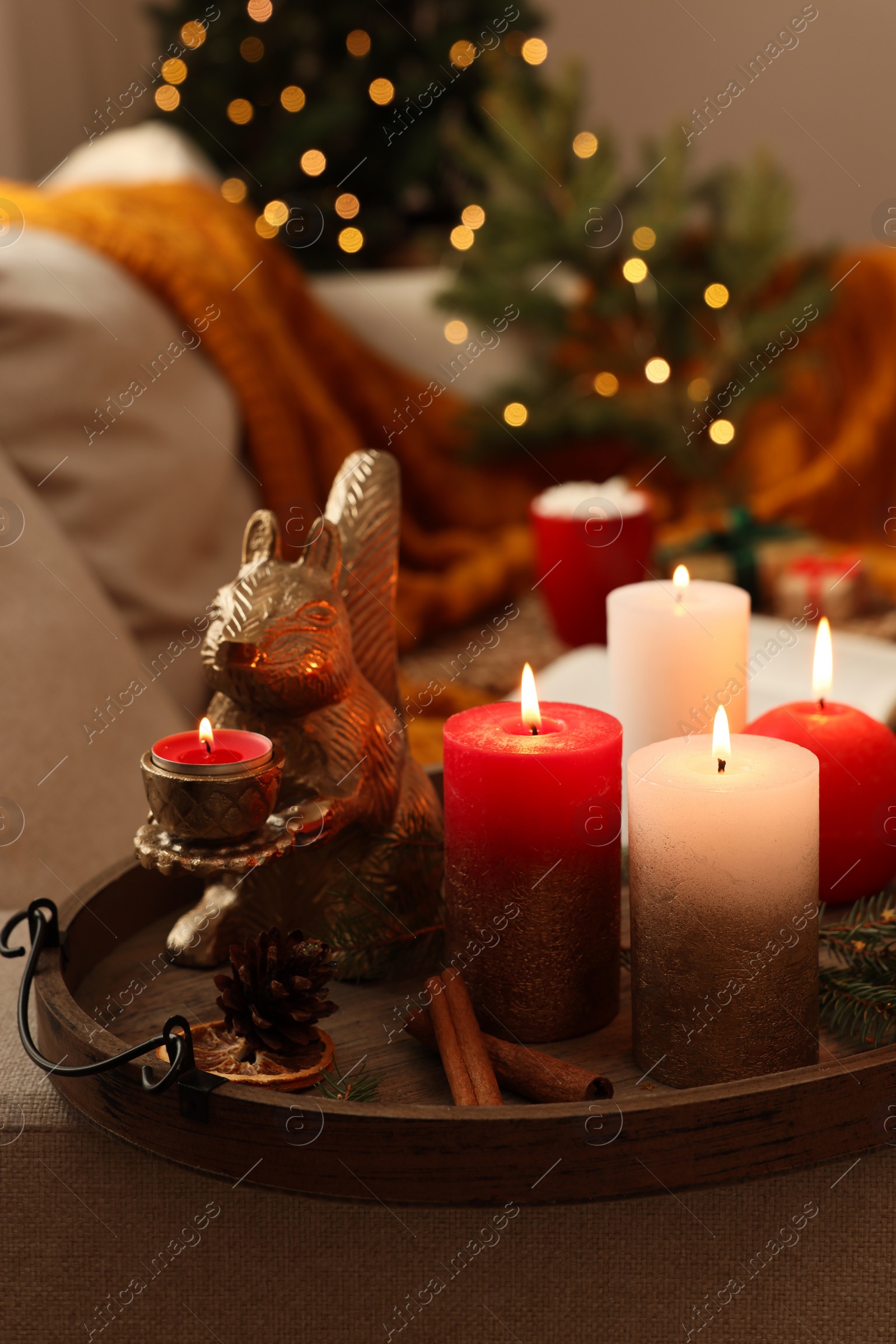 Photo of Tray with beautiful burning candles and Christmas decor on sofa at home