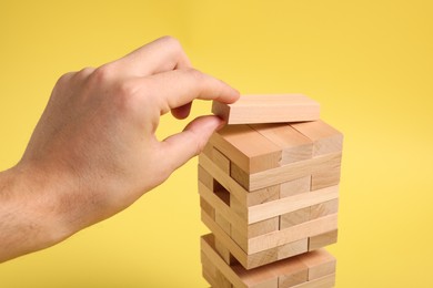 Playing Jenga. Man building tower with wooden blocks on yellow background, closeup