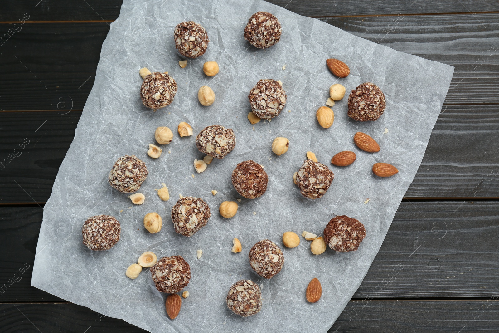 Photo of Delicious sweet chocolate candies and nuts on dark wooden table, top view