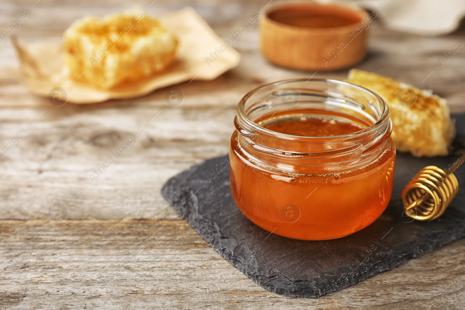 Photo of Glass jar with sweet honey and dipper on wooden table, closeup