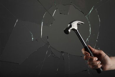 Woman breaking window with hammer on grey background, closeup