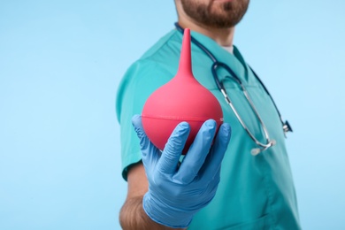 Photo of Doctor holding pink enema on light blue background, closeup