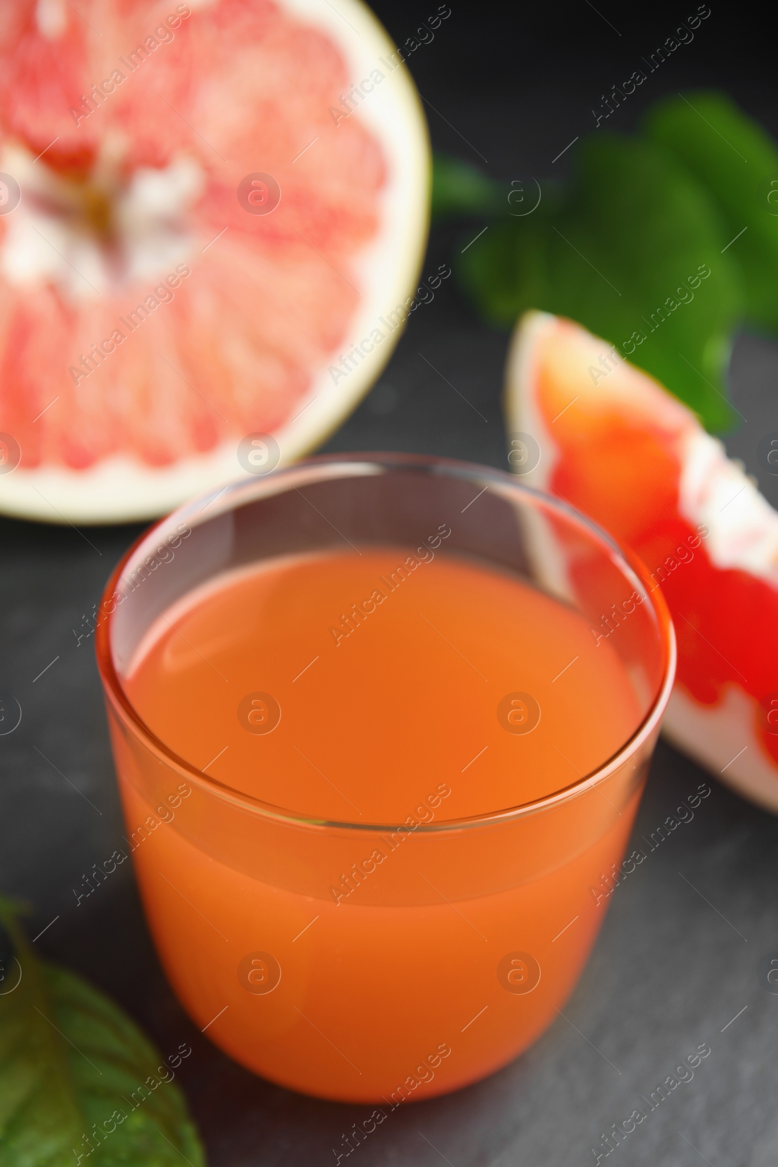 Photo of Glass of pink pomelo juice and green leaves on black table