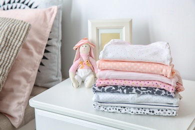 Photo of Toy bunny and stack of stylish child clothes on table indoors