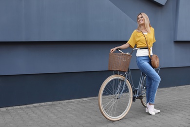 Woman with bicycle on street near gray wall