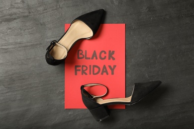 Photo of Elegant shoes and sheet of red paper with words Black Friday on dark background, flat lay