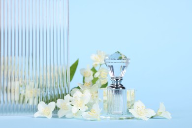 Photo of Aromatic perfume in bottle and beautiful jasmine flowers on light blue background, closeup