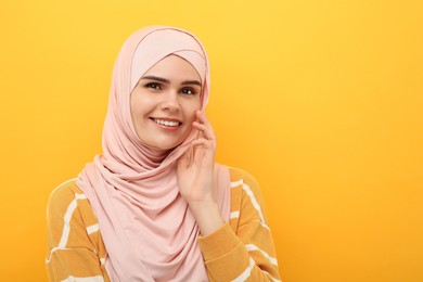Photo of Portrait of Muslim woman in hijab on orange background, space for text