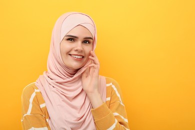 Portrait of Muslim woman in hijab on orange background, space for text