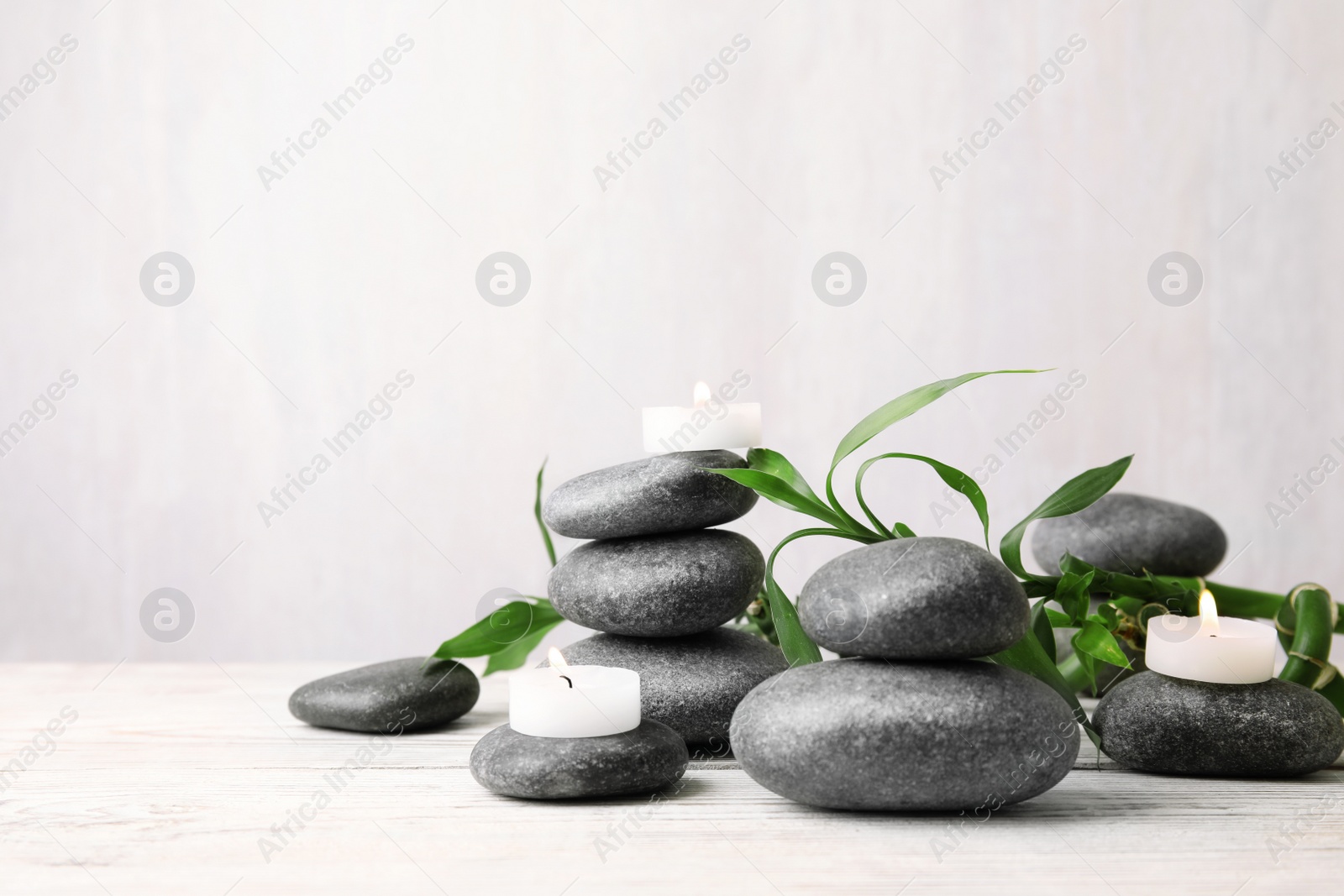 Photo of Composition with zen stones, bamboo and lighted candles on table against light background. Space for text