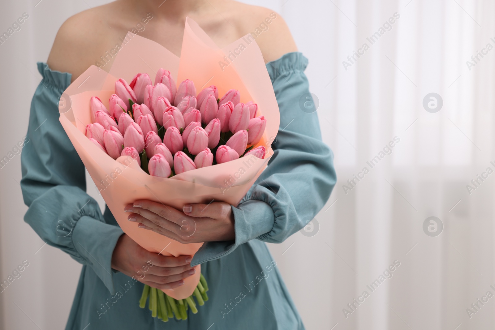 Photo of Woman holding bouquet of pink tulips indoors, closeup. Space for text