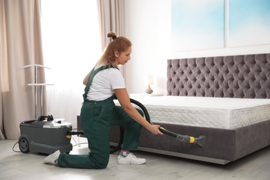 Photo of Janitor cleaning bed with professional equipment in room