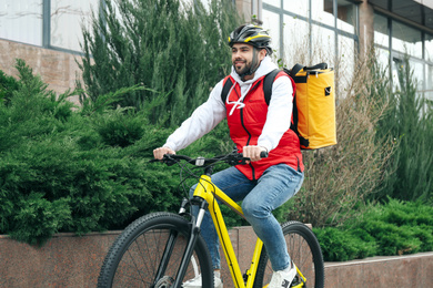 Courier with thermo bag riding bicycle outdoors. Food delivery service