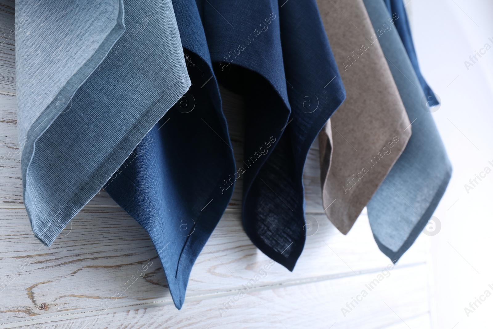 Photo of Different kitchen napkins hanging on white wooden wall, closeup