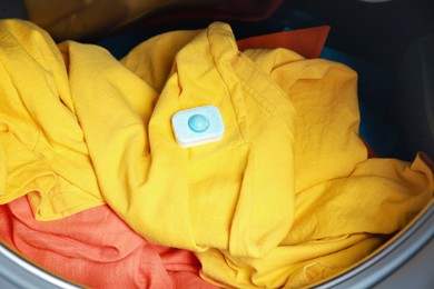 Photo of Water softener tablet on clothes in washing machine, closeup