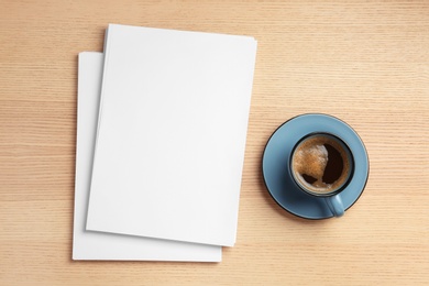 Photo of Blank paper sheets for brochure and cup of coffee on wooden background, flat lay. Mock up