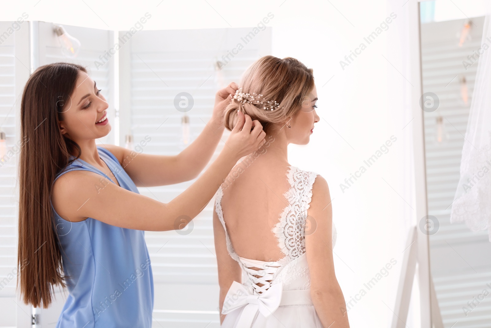 Photo of Fashion stylist preparing bride before her wedding indoors